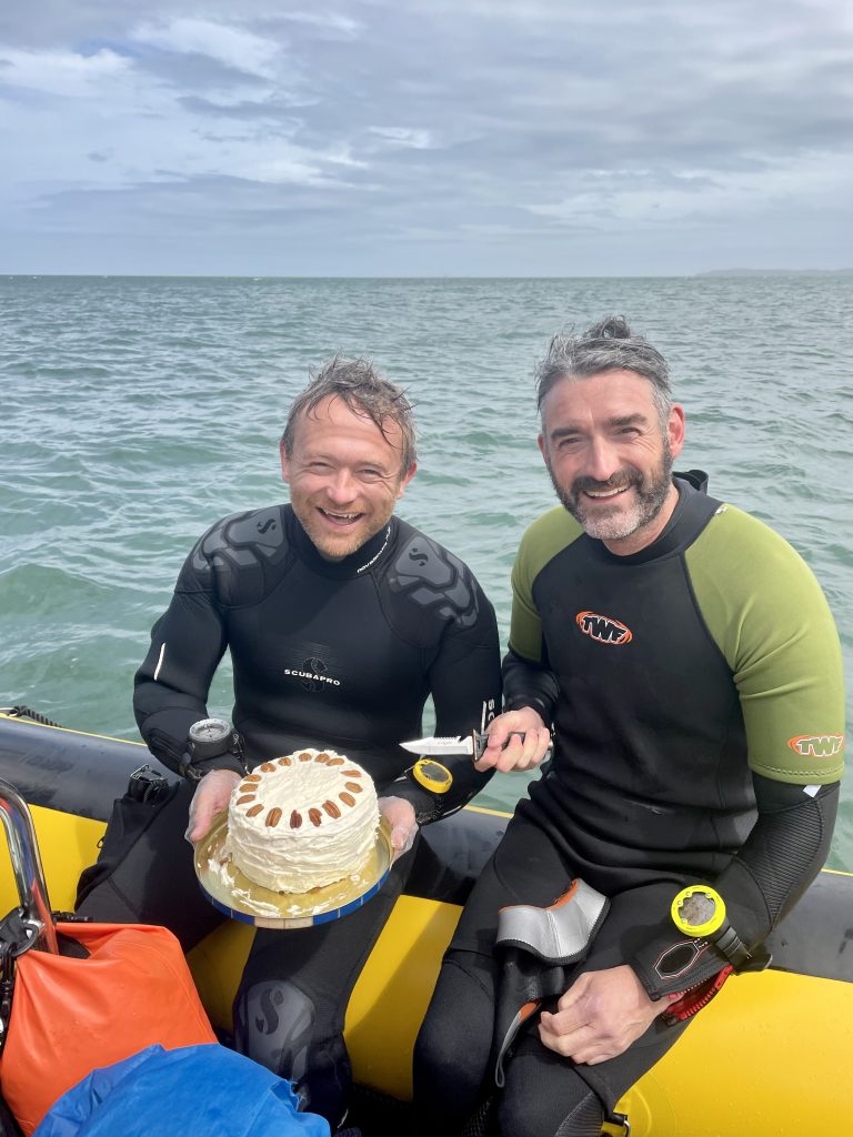 Two divers on a dive boat with a cake