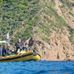 Clidive's yellow RHIB picking up divers on the blue Mediterranean with the sunlit rocky coast behind.