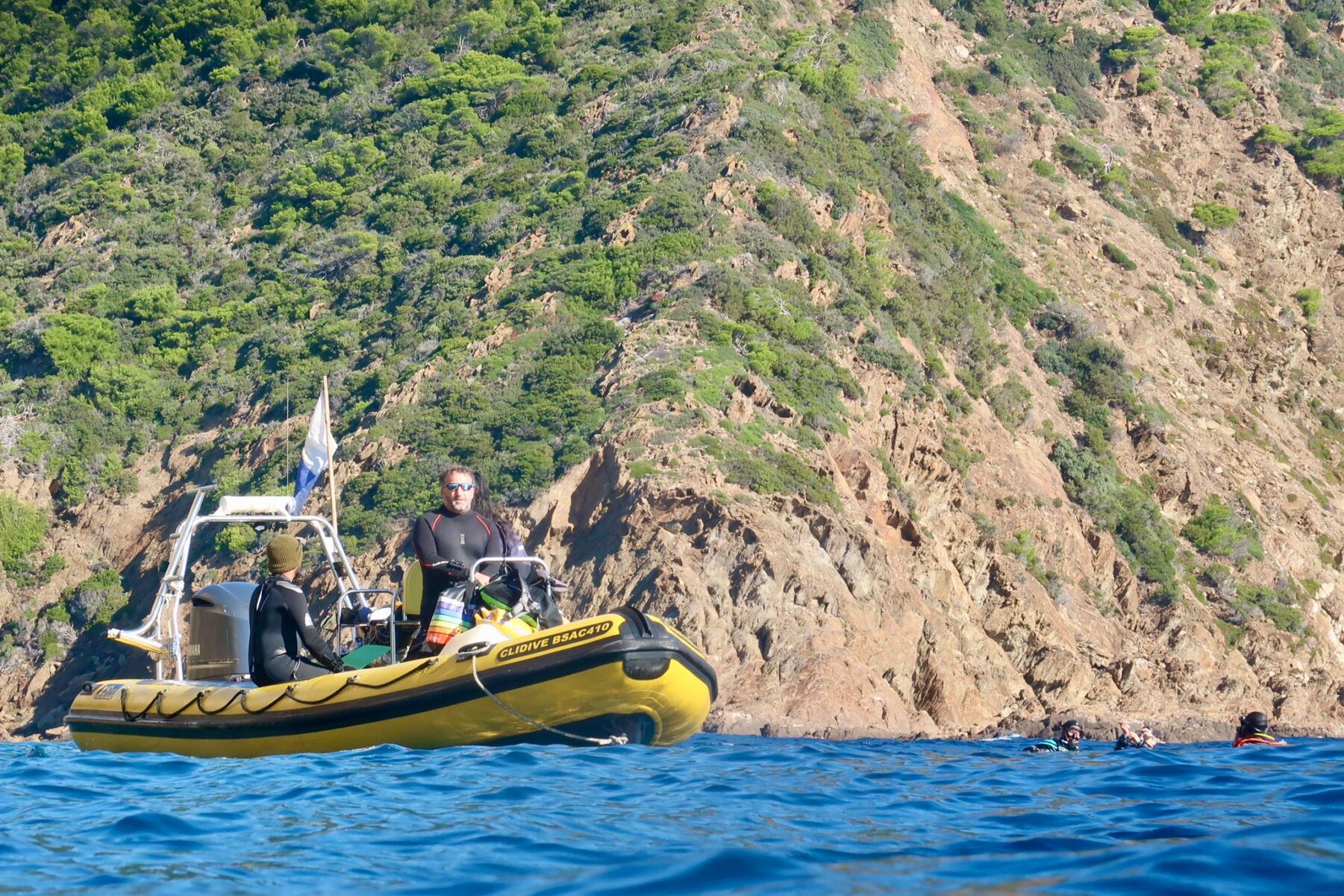 Clidive's yellow RHIB picking up divers on the blue Mediterranean with the sunlit rocky coast behind.
